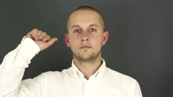 Un joven guapo con una camisa blanca, se despide y le da la mano. Retrato sobre fondo gris . — Vídeo de stock