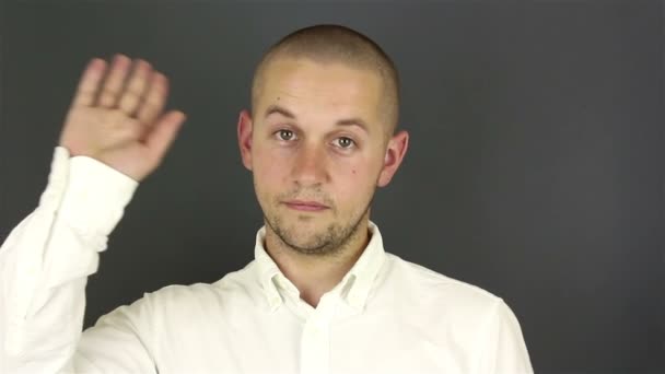 Un joven guapo con una camisa blanca, se despide y le da la mano. Retrato sobre fondo gris . — Vídeo de stock