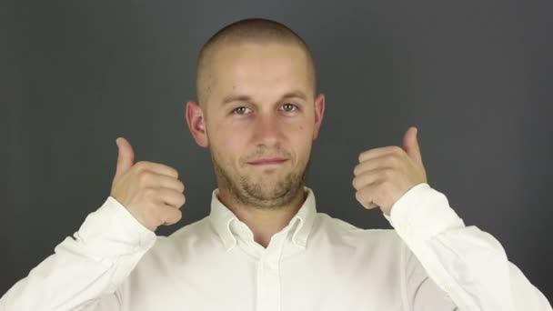 Divertido chico guapo sonríe y muestra el pulgar hacia arriba con ambas manos. Retrato sobre fondo gris . — Vídeos de Stock