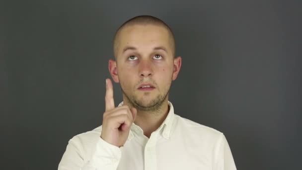 Un tipo gracioso y guapo con una camisa blanca muestra su dedo índice y asiente con la cabeza. Retrato sobre fondo gris . — Vídeo de stock