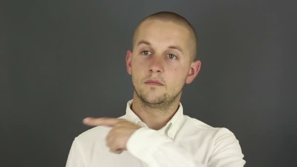Grappige, knappe man in een wit shirt laat zijn wijsvinger naar de zijkant zien. Portret op een grijze achtergrond. — Stockvideo