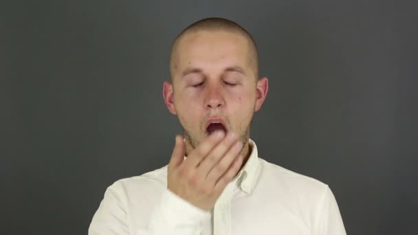 Young handsome guy actively yawns and covers his mouth with his hand. A young guy in a white shirt yawns in a meeting and covers his mouth with his hand. — Stock Video