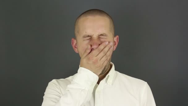 若いハンサムな男が積極的にあくびをし、彼の手で口をカバーしています。白いシャツを着た若い男が会議であくびをし、手で口を覆います. — ストック動画