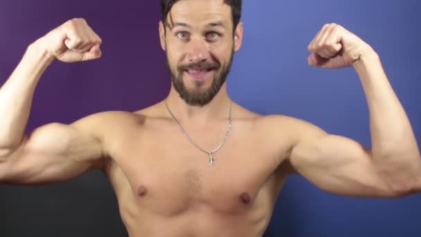 A funny young guy with a naked torso shows a thumb up. A funny guy with a naked torso shows his muscles, smiles and grimaces while looking at the camera. — Stock Video