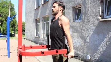 Çekici bir genç barlarda şınav çeker. Genç ve güçlü bir adam spor sahasında çalışıyor..