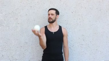Genç ve çekici bir adam üç beyaz topla hokkabazlık yapıyor. Genç adam hokkabazlık eğitimi alıyor..