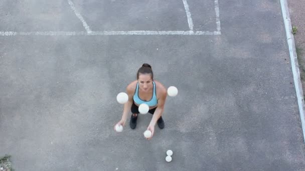 Un malabarista profesional hace malabares con bolas blancas. Una chica atractiva malabarista entrena sus habilidades de malabares. Una actriz de circo profesional hace malabares con bolas blancas en la calle . — Vídeos de Stock