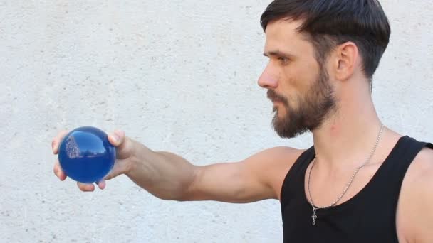 Молодий привабливий хлопець займається контактним жонглюванням. Чоловік жонглює блакитну прозору кульку . — стокове відео