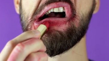 Sakallı genç bir adam dudaklarını kırmızı rujla boyuyor. Sakallı bir adamın yakın çekimi, parlak rujla dudaklarını boyadı. Sakallı bir adam dudaklarına kırmızı ruj sürer, gülümser ve dudaklarına şaplak atar..