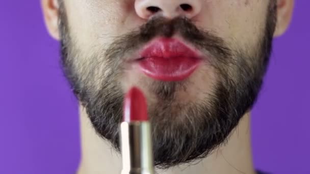 Un tânăr cu barbă îşi vopseşte buzele cu ruj roşu. Apropiat de un bărbat cu barbă, a pictat buze cu ruj strălucitor. Un bărbat cu barbă își pune rujul roșu pe buze, zâmbește și își lovește buzele . — Videoclip de stoc