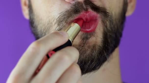 A young guy with a beard paints his lips with red lipstick. Close-up of a bearded man, he painted lips with bright lipstick. A bearded man puts red lipstick on his lips, smiles and smacks his lips. — Stock Video