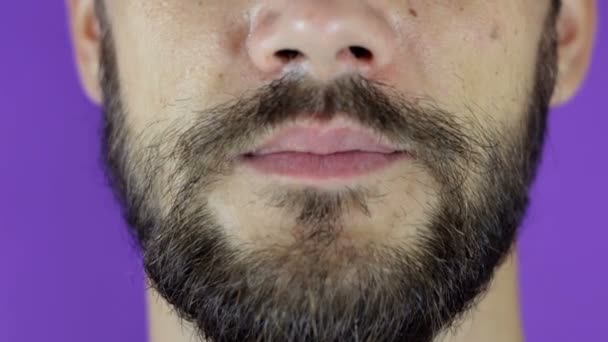 Jóképű szakállas férfi a kamerába néz és megmutatja a nyelvét. Közelkép egy fiatal szakállas fickóról, aki örömmel nyalogatja az ajkait.. — Stock videók