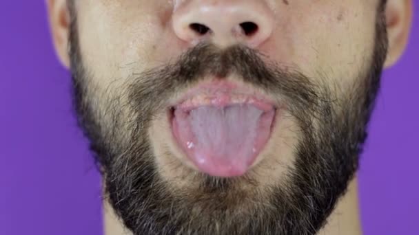 Knappe man met een baard kijkt naar de camera en laat zijn tong zien. close-up van een jong baard guy likt zijn lippen met plezier. — Stockvideo