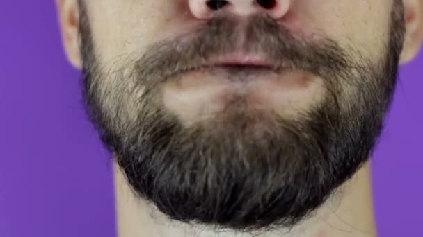 Jóképű szakállas férfi a kamerába néz és megmutatja a nyelvét. Közelkép egy fiatal szakállas fickóról, aki örömmel nyalogatja az ajkait.. — Stock videók