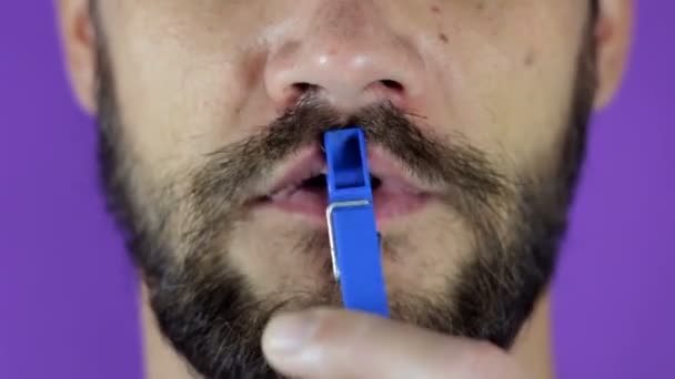 Крупный план портрета молодого бородатого парня, который щекочет губы прищепкой. — стоковое видео