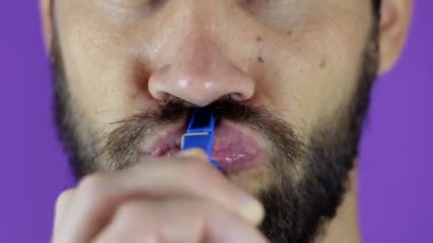 Close up portrait of a young bearded guy who pinches his lips with a clothespin. — Stock Video