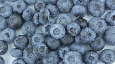 Beyaz arka planda olgun sulu yaban mersinlerinin yakın çekimi. Tabakta taze organik yaban mersini var. Taze sulu yaban mersinli yakın çekim rotasyonu.