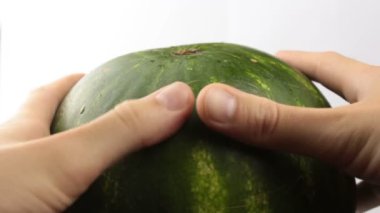 Adam karpuzun olgunluğunu kontrol ediyor, parmaklarını ona vuruyor. Genç bir adamın yeşil çizgili bir karpuzu tıklayarak olgunluğunu ölçtüğü yakın plan. Su damlaları sulu bir karpuzun kabuğundan aşağı akar..