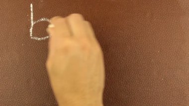 Erkek bir elin yakın çekimi, kelimeleri okula tebeşirle kahverengi bir karatahtaya yazıyor. Bir adam kelimeleri okula tebeşirle kahverengi bir tahtaya yazıyor..