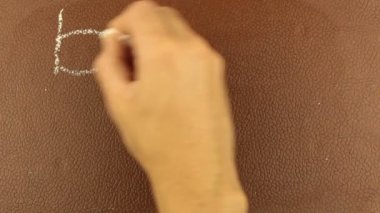 Erkek bir elin yakın çekimi, kelimeleri okula tebeşirle kahverengi bir karatahtaya yazıyor. Bir adam kelimeleri okula tebeşirle kahverengi bir tahtaya yazıyor..