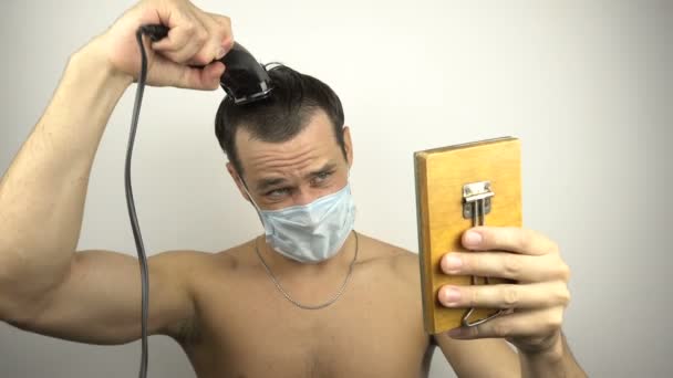 Młody Przystojniak Masce Ochronnej Obcina Sobie Włosy Elektrycznym Przycinaczem Podczas — Wideo stockowe