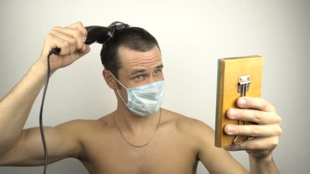 Młody Przystojniak Masce Ochronnej Obcina Sobie Włosy Elektrycznym Przycinaczem Podczas — Wideo stockowe