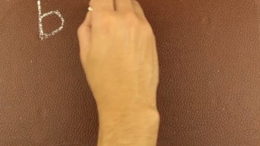 Erkek bir elin yakın çekimi, kelimeleri okula tebeşirle kahverengi bir karatahtaya yazıyor. Bir adam kelimeleri okula tebeşirle kahverengi bir tahtaya yazıyor..