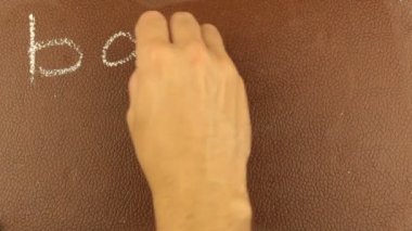 Erkek bir elin yakın çekimi, kelimeleri okula tebeşirle kahverengi bir karatahtaya yazıyor. Bir adam kelimeleri okula tebeşirle kahverengi bir tahtaya yazıyor..