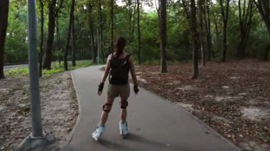 Genç çekici kız parkta paten kayıyor. Genç mutlu kız yaz parkında paten kaymaktan hoşlanıyor..