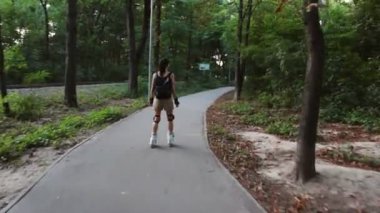 Genç çekici kız parkta paten kayıyor. Genç mutlu kız yaz parkında paten kaymaktan hoşlanıyor..