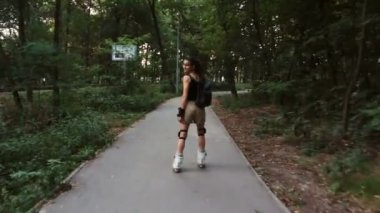 Genç çekici kız parkta paten kayıyor. Genç mutlu kız yaz parkında paten kaymaktan hoşlanıyor..