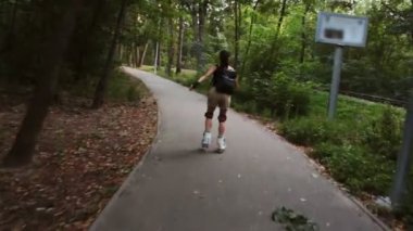 Genç çekici kız parkta paten kayıyor. Genç mutlu kız yaz parkında paten kaymaktan hoşlanıyor..
