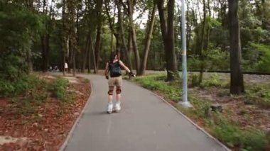 Genç çekici kız parkta paten kayıyor. Genç mutlu kız yaz parkında paten kaymaktan hoşlanıyor..