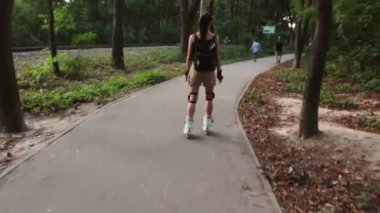 Genç çekici kız parkta paten kayıyor. Genç mutlu kız yaz parkında paten kaymaktan hoşlanıyor..