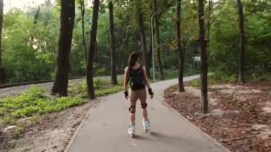  Genç çekici kız parkta paten kayıyor. Genç mutlu kız yaz parkında paten kaymaktan hoşlanıyor..