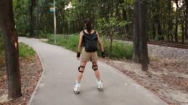 Genç çekici kız parkta paten kayıyor. Genç mutlu kız yaz parkında paten kaymaktan hoşlanıyor..