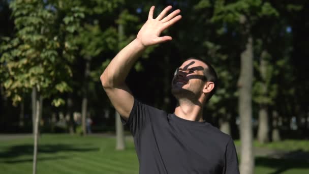 En ung attraktiv kille kisar på solen och täcker ansiktet med handen. Slow motion porträtt av en ung kille som ler brett och kisar på solen. — Stockvideo