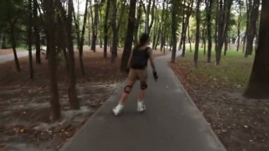 Genç çekici bayan parkta paten kayıyor. Genç mutlu kadın yaz parkında paten kaymanın tadını çıkarıyor..