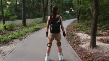 Genç çekici bayan parkta paten kayıyor. Genç mutlu kadın yaz parkında paten kaymanın tadını çıkarıyor..