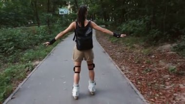 Genç çekici bayan parkta paten kayıyor. Genç mutlu kadın yaz parkında paten kaymanın tadını çıkarıyor..