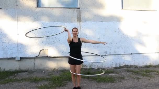Eine attraktive Frau, eine Zirkusartistin, dreht Hula-Hoop-Reifen auf der Straße und verbessert ihre Fähigkeiten. Straßenkünstler übt Hula-Hoop-Spinning.