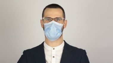 Tıbbi koruyucu maskeli genç ve başarılı iş adamı müşterileri karşılarken elini sallıyor..