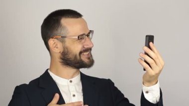 Genç ve başarılı bir iş adamı, akıllı telefonuyla bir video sohbetinde ortaklarıyla konuşuyor. Genç yakışıklı işadamı bir video görüşmesi yaptı..