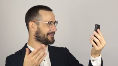 Genç ve başarılı bir iş adamı, akıllı telefonuyla bir video sohbetinde ortaklarıyla konuşuyor. Genç yakışıklı işadamı bir video görüşmesi yaptı..