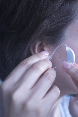 Sağır orta yaşlı Bayan modern dijital teknoloji işitme cihazı kulağına giyiyor.