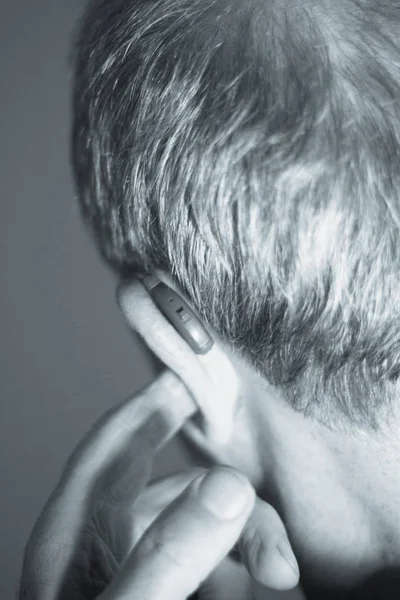 聴覚障害者高齢者男の耳で身に着けている現代デジタル高技術補聴器 — ストック写真