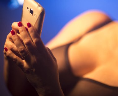 Seksi büyük göğüslü kadın erotik iç çamaşırlarıyla cep telefonu kullanıyor..