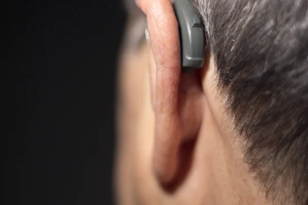 Deaf senior citizen man wearing modern digital high technology hearing aid in ear.