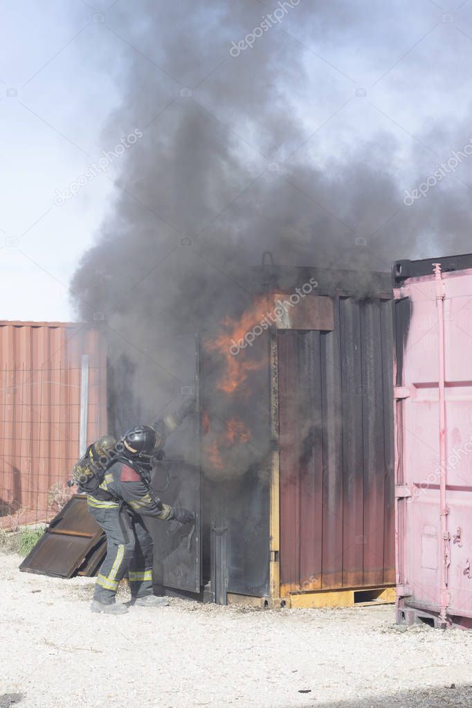 Firefighter putting out fire training station extinguisher backdraft emergency safety drill with ship container.