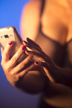 Seksi büyük göğüslü kadın erotik iç çamaşırlarıyla cep telefonu kullanıyor..